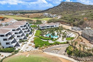 A resort with modern architecture, a pool area, and a golf course in the background.