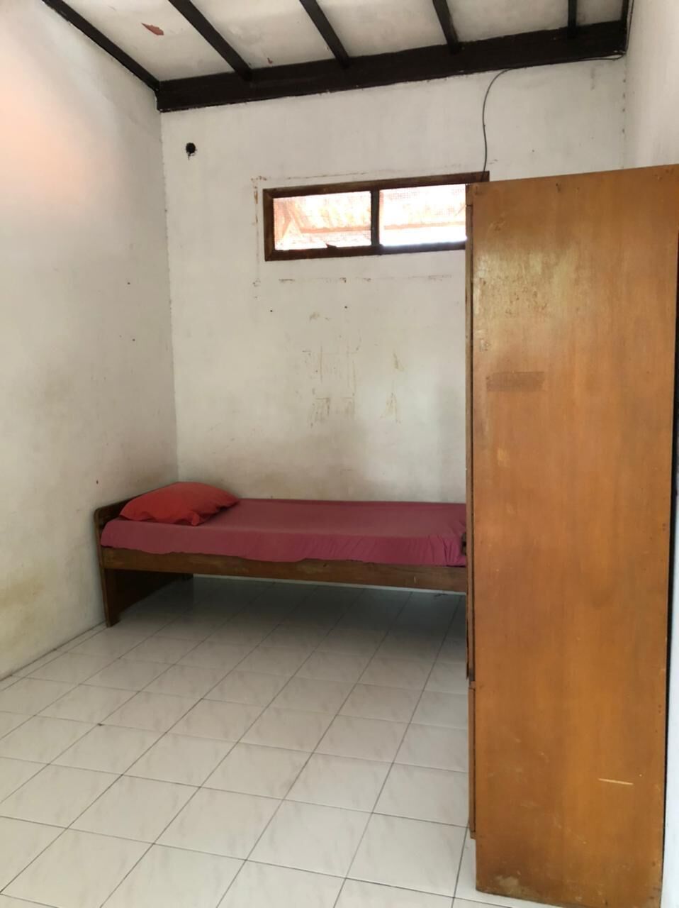 Una habitación pequeña con una cama individual, una ventana y una puerta de madera.