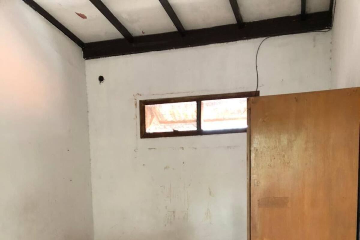 A small room with a single bed, a window, and a wooden door.
