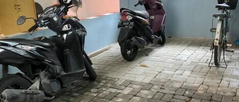 A covered parking area with a brick floor, a scooter, and a bicycle.