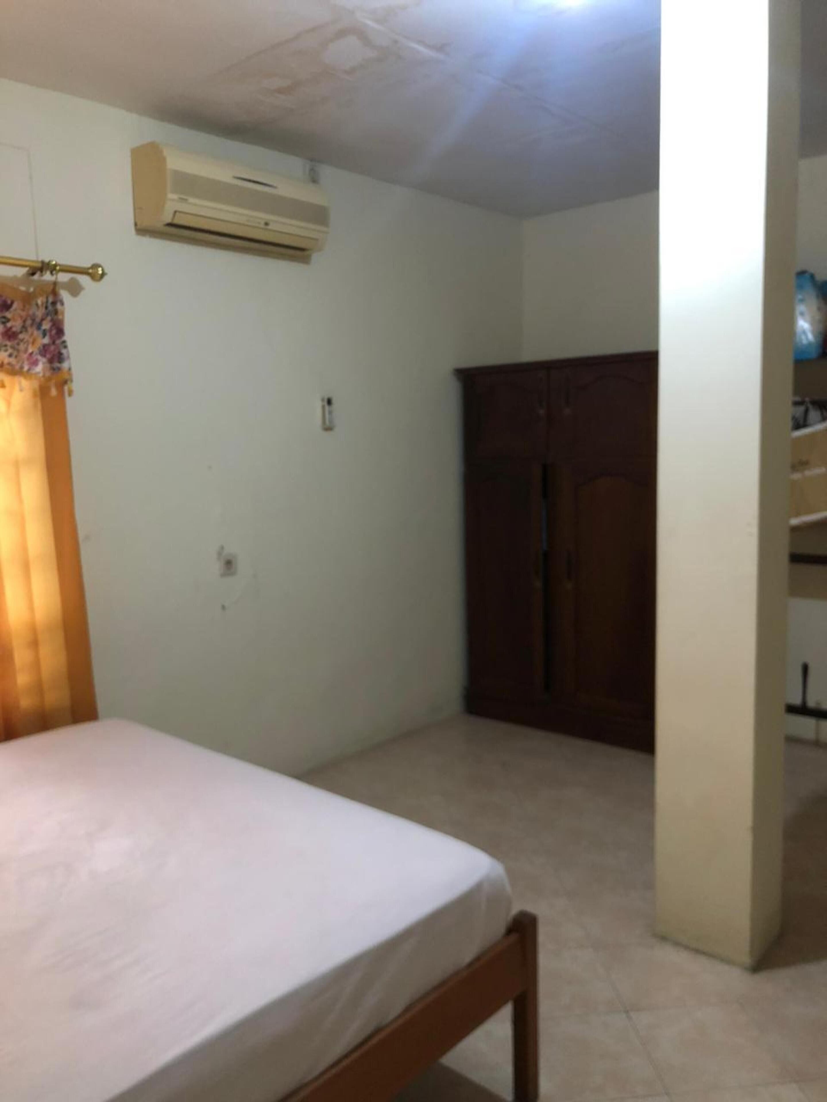 Un dormitorio con cama, aire acondicionado, armario y una puerta que da a otra habitación.