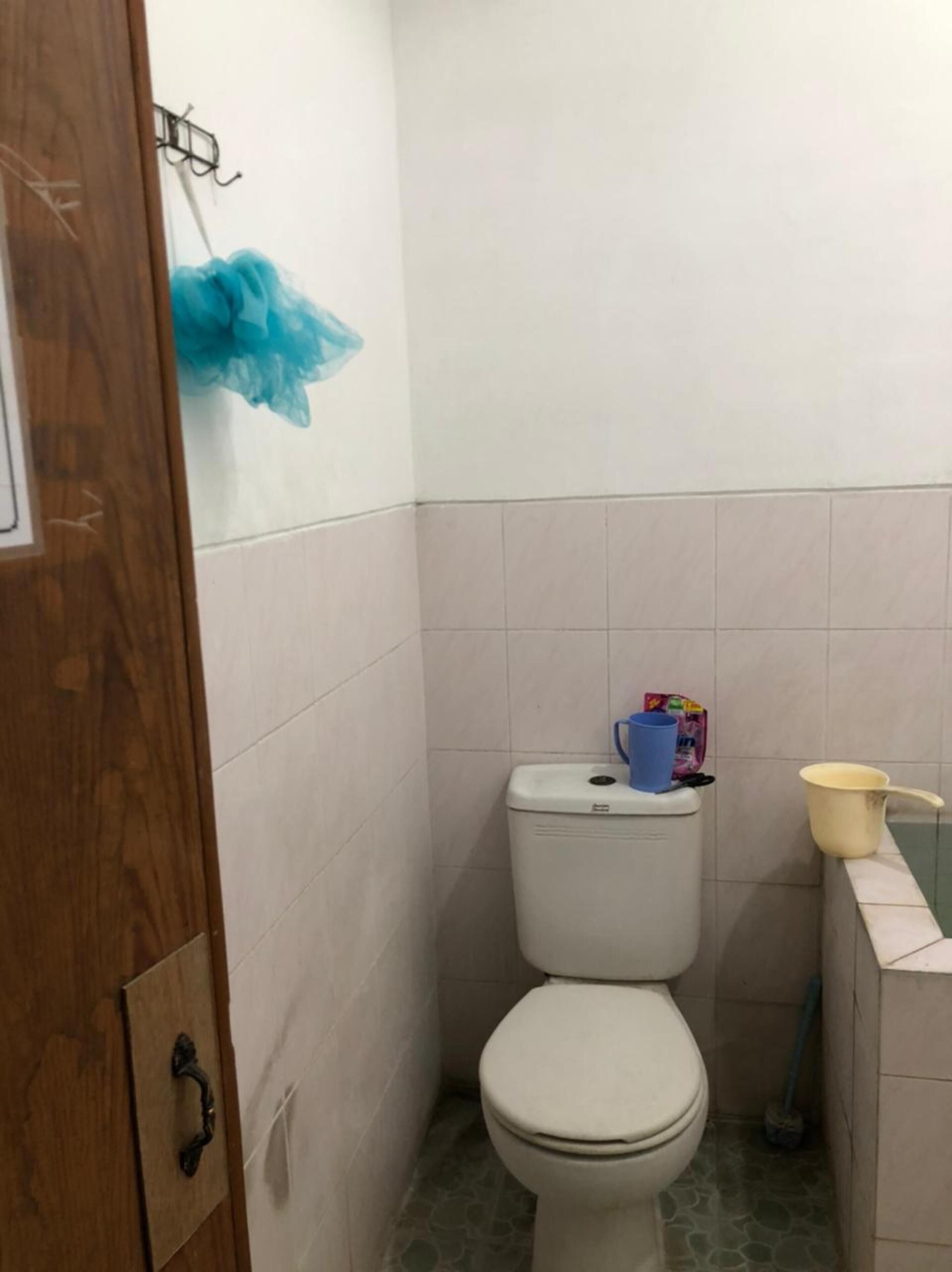 A small bathroom with a toilet, a blue trash bag, a yellow bucket, and a broom.