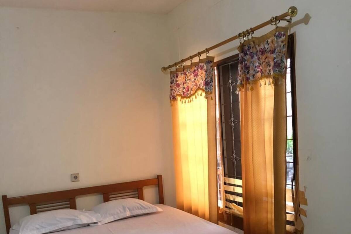 A single bed with a wooden frame, a plain white mattress, and a curtain with floral patterns.