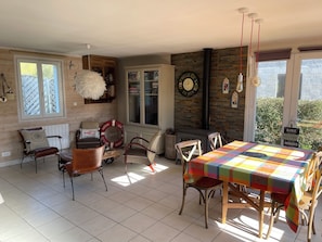 Un'accogliente zona pranzo con pavimento piastrellato, sedie di legno, un tavolo ricoperto da una tovaglia colorata, un camino e un'ampia finestra con vista su piante.