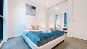 Un dormitorio moderno con una cama grande, una mesita de noche, un espejo y un cuadro en la pared.
