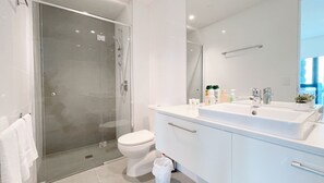 Un baño moderno con ducha de vidrio, inodoro blanco y tocador con lavamanos y espejo.