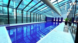 Una piscina interior con paredes de vidrio transparente, suelo de baldosas y un cartel que indica una profundidad de 1,4 metros, prohibido bucear.