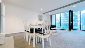 Uma sala de jantar moderna com uma mesa e cadeiras brancas, vista para a cidade através de grandes janelas e decoração minimalista.