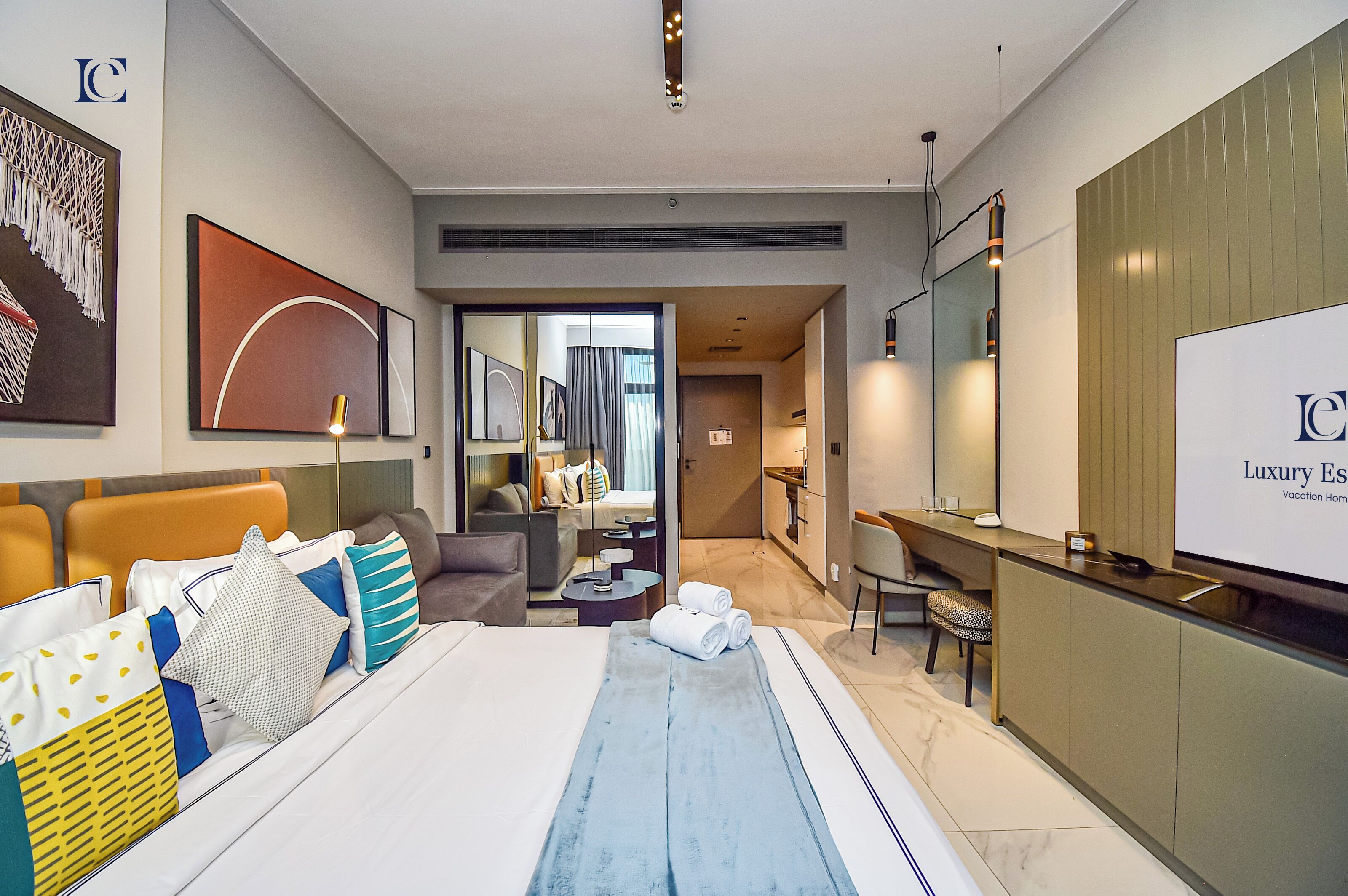 A modern hotel room with a large bed, a desk, and a view into the living area.