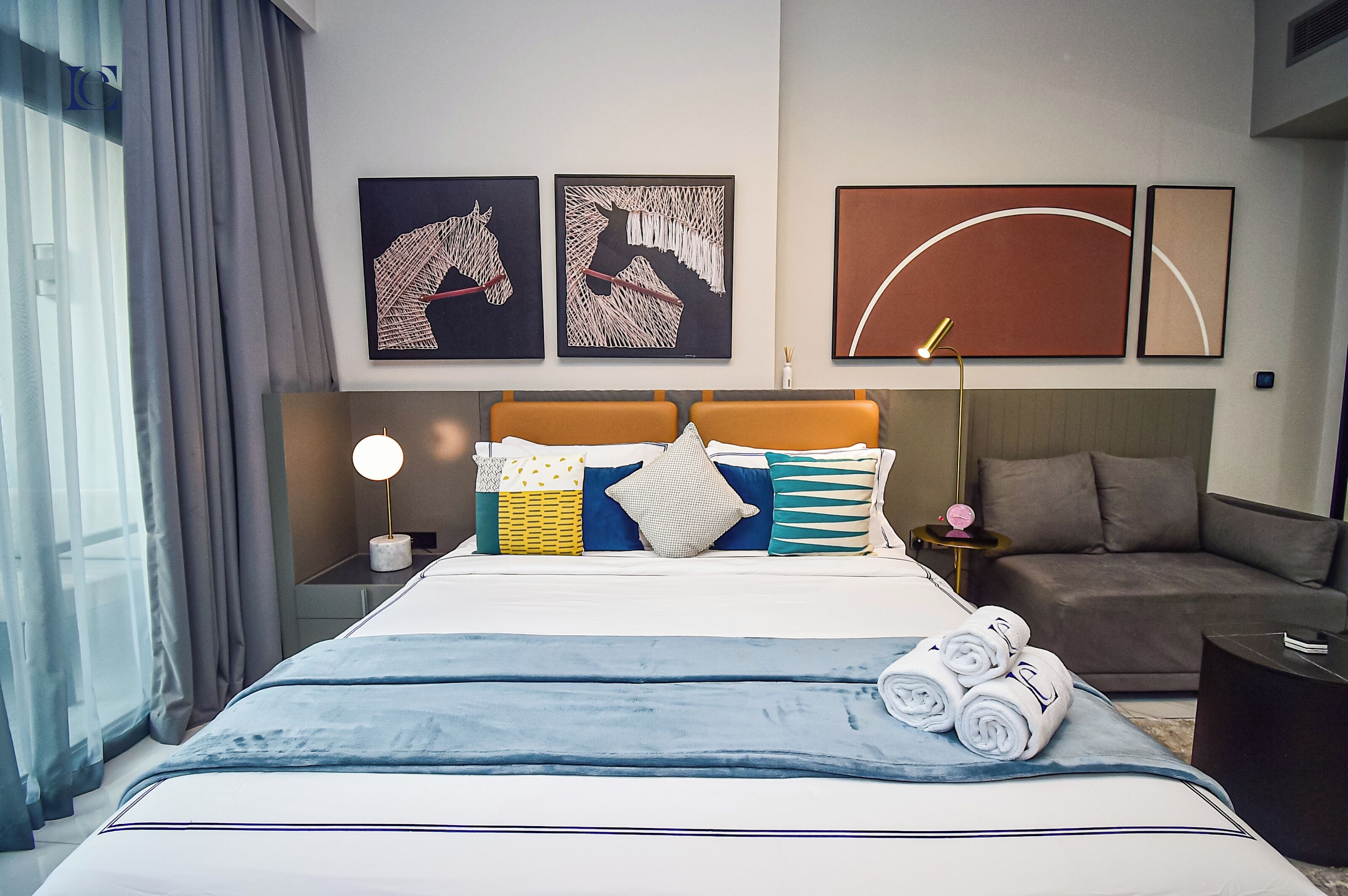 A modern hotel room with a large bed, a sofa, and artwork on the walls.