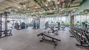 Uma academia espaçosa com diversos equipamentos de exercício, grandes janelas e um design moderno de teto industrial.