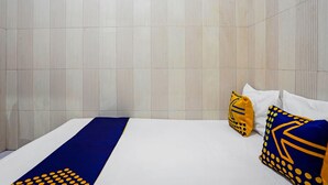Une chambre d’hôtel avec un lit, des oreillers blancs et un chemin de table bleu et jaune.