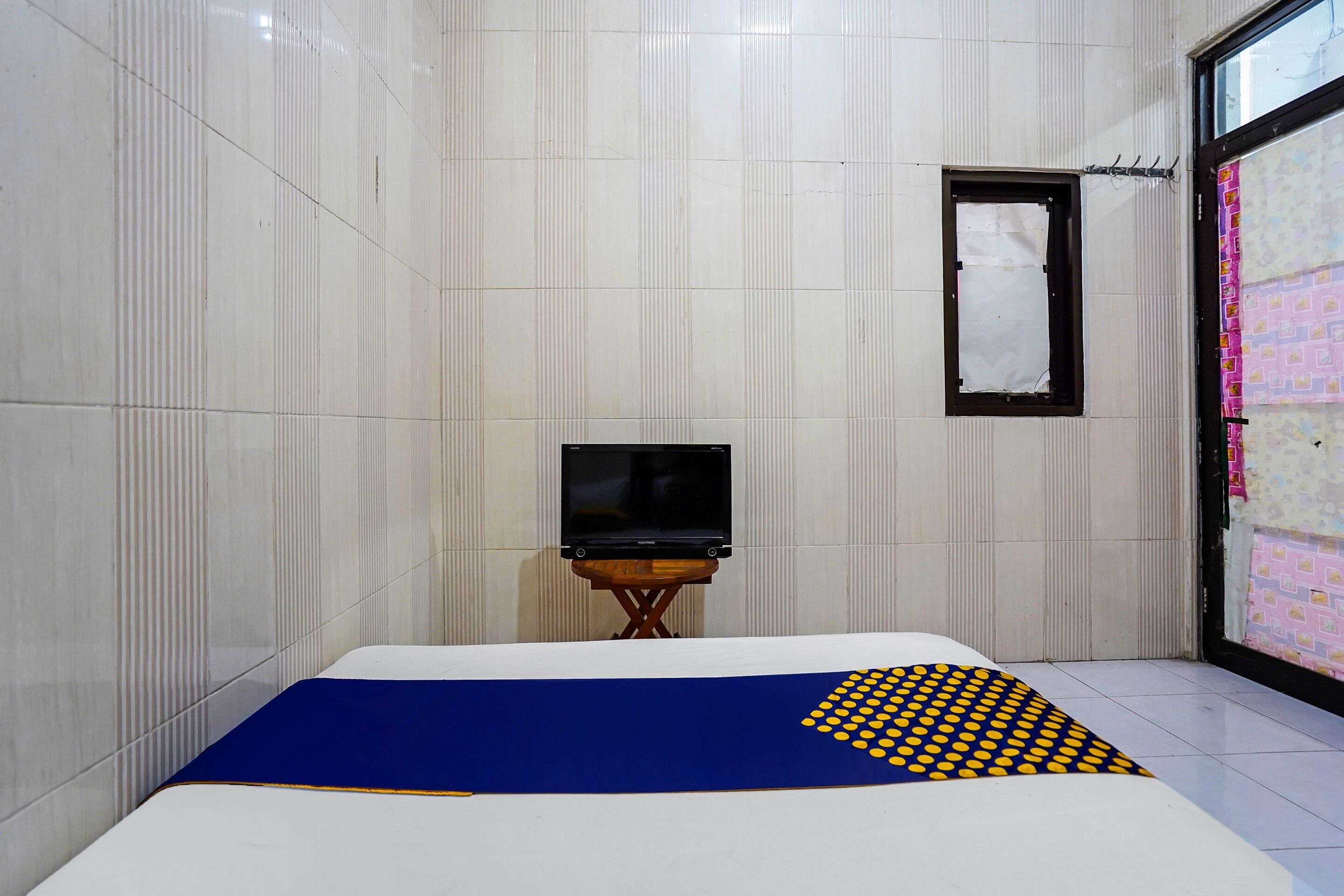 A hotel room with a bed, a TV on a small table, and a window with a view of the outside.