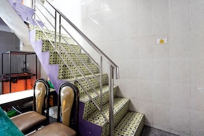 Stairs lead to an upper level, flanked by a metal railing and a seating area with cushioned chairs and a glass-topped table.