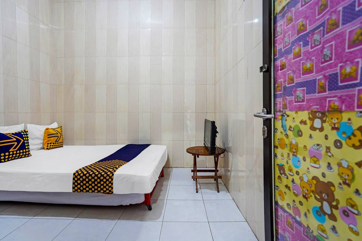 Une chambre d’hôtel avec un lit, des oreillers, un téléviseur posé sur une petite table et une porte aux couleurs vives.