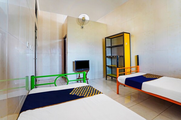 Two single beds with matching bedspreads, a TV, and a green chair sit in a room with a large window and a ceiling fan.