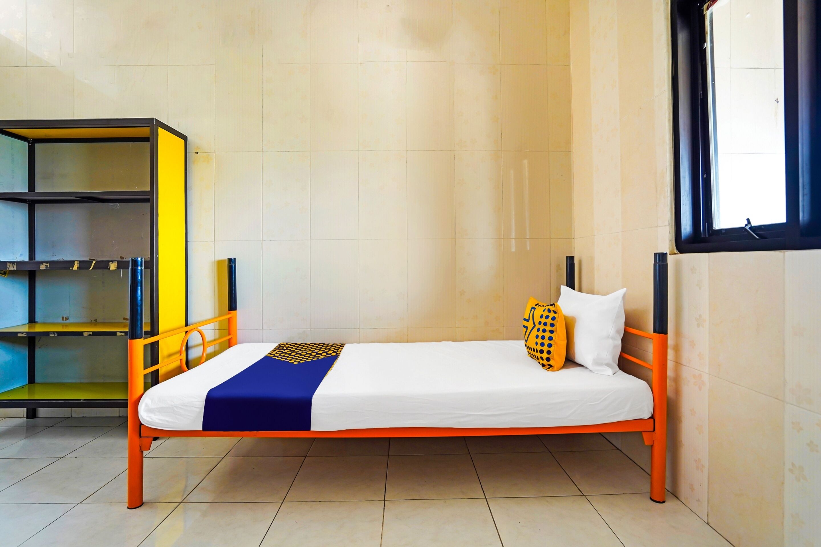 A single bed with an orange frame, white bedding, and a blue and yellow blanket.