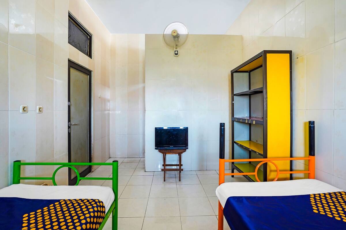 Une chambre d’hôtel avec deux lits, un téléviseur posé sur un meuble et une bibliothèque.
