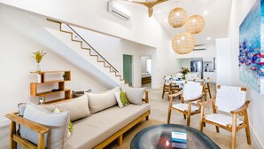 A modern living room with a sofa, coffee table, and chairs, a staircase, and a kitchen area. - Newly Renovated, Beachfront, 3 bed Condo on Exclusive Langosta Beach! (Tamarindo)