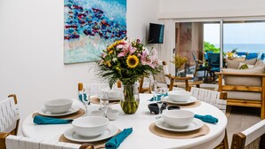A dining area with a table set for four, a vase of flowers, and a large painting on the wall. - Newly Renovated, Beachfront, 3 bed Condo on Exclusive Langosta Beach! (Tamarindo)