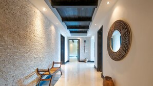 A hallway with a textured wall, a wooden bench, a decorative mirror, and a woven basket. - Beautiful 3 Bedroom Condo (Punta de Mita)