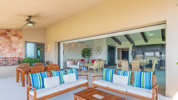 A spacious outdoor seating area with wooden furniture and striped cushions, a stone wall, and a view into the interior. - Beautiful 3 Bedroom Condo (Punta de Mita)