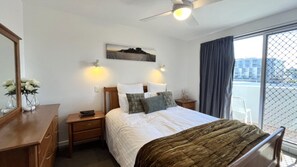 A hotel room with a bed, a nightstand, a dresser, a ceiling fan, and a window with a view of buildings. - Pumicestone Chase 5 Absolute Water Front (BULCOCK BEACH)