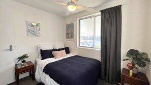 A bedroom with a bed, a nightstand, a window with curtains, and a ceiling fan. - Pumicestone Chase 5 Absolute Water Front (BULCOCK BEACH)