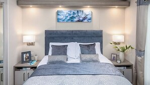 A bedroom with a bed, nightstands, a headboard, wall art, and a bedside table with a lamp.