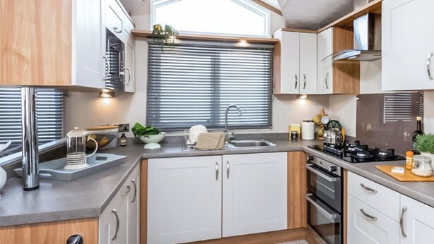 A compact kitchen with white cabinets, a built-in oven, a gas stove, and a window with blinds.