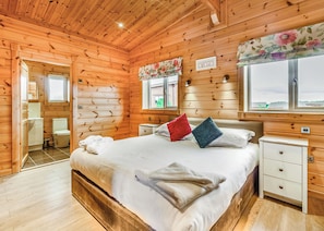 A wooden cabin bedroom with a bed, bedside tables, a window with a view, and a bathroom with a toilet and sink. - 2 bedroom accommodation in Withernsea (Withernsea)