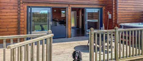 Une cabane en bois avec une terrasse, un chien sur un tapis bleu et un jacuzzi.