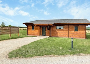 A wooden cabin with a gravel driveway and a grassy lawn.