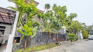 A residential area with a paved driveway, a gated entrance, and a variety of tropical plants.