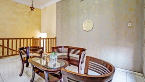 A dining area with a round glass table and wooden chairs, a staircase with a railing, and a wall with floral wallpaper.