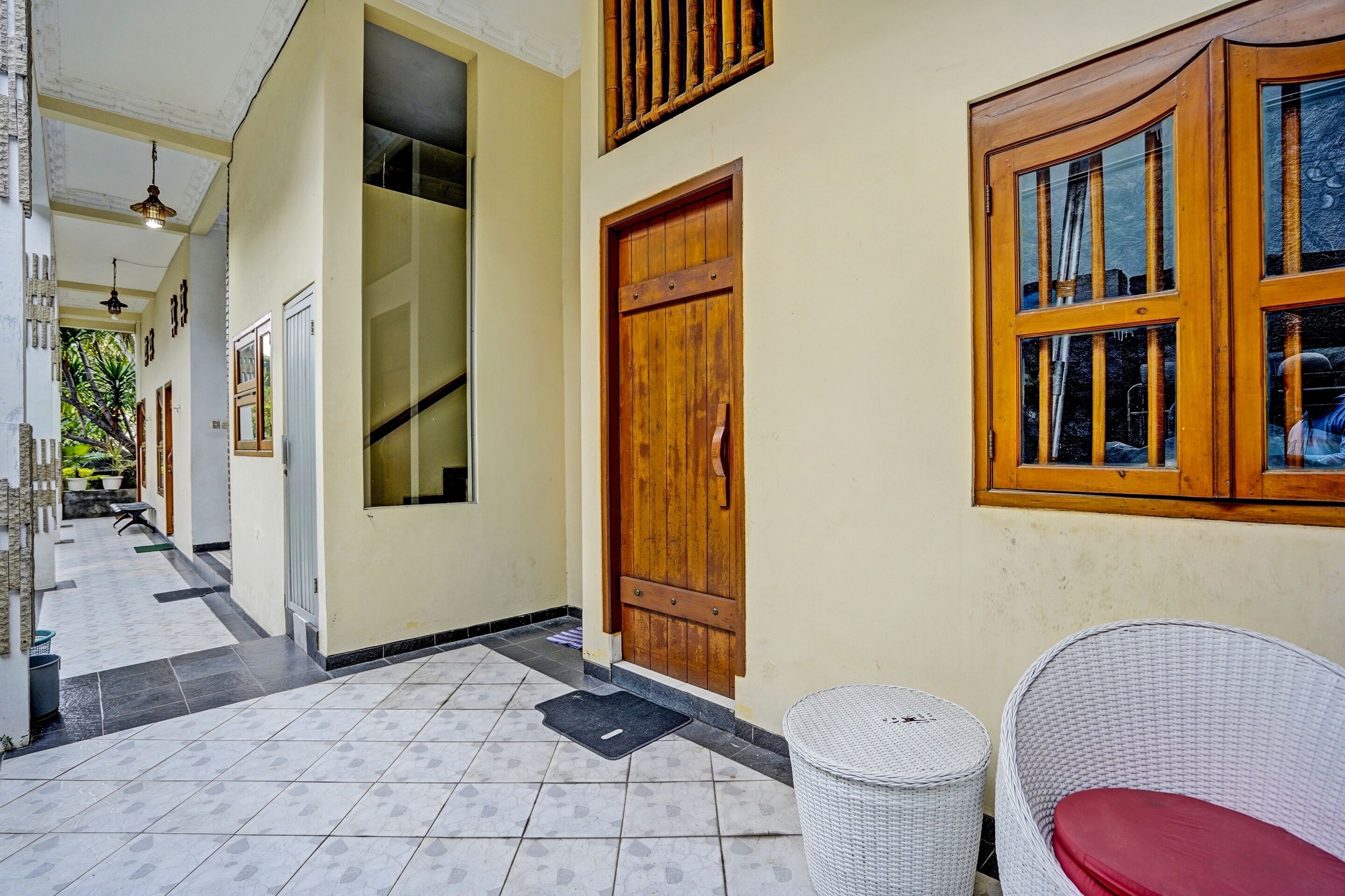 A hallway with a wooden door, a wicker chair, and a trash bin.