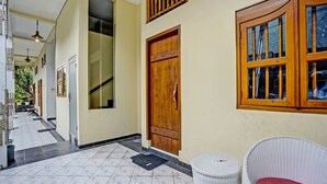 A hallway with a wooden door, a wicker chair, and a trash bin.
