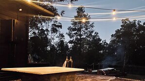 A rustic outdoor setting with a large bathtub, gravel ground, and string lights overhead. - Little Olive Eco Cabin on a private dam.. Perfect for a relaxing weekend away! (Parklands)
