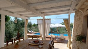 Un espace extérieur abrité comprenant une piscine, des meubles en bois et une table sur laquelle est posé un panier de fruits.