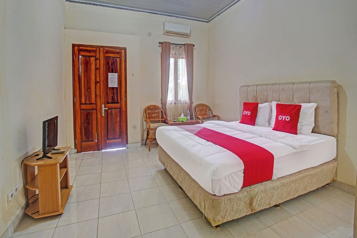 Une chambre d’hôtel avec un grand lit, deux chaises, un bureau en bois et un appareil de climatisation.