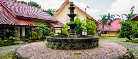 A courtyard with a stone fountain, surrounded by buildings with red-tiled roofs.