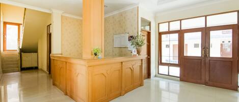 A spacious lobby with a wooden reception desk, a large wooden door, and a tiled floor.