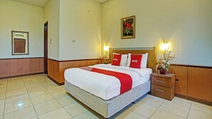 Een hotelkamer met een groot bed, een houten hoofdbord, twee nachtkastjes met lampen, een ingelijst schilderij aan de muur en een pot met een plant op het nachtkastje.
