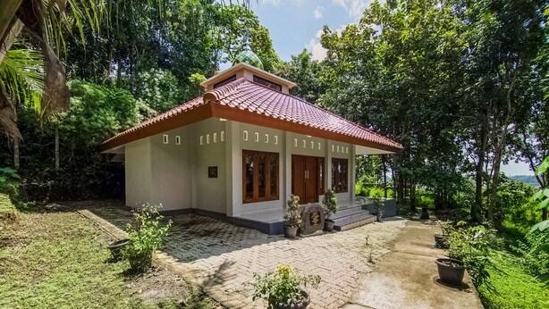 Een klein huis met pannendak, omringd door weelderige begroeiing en een geplaveid pad.