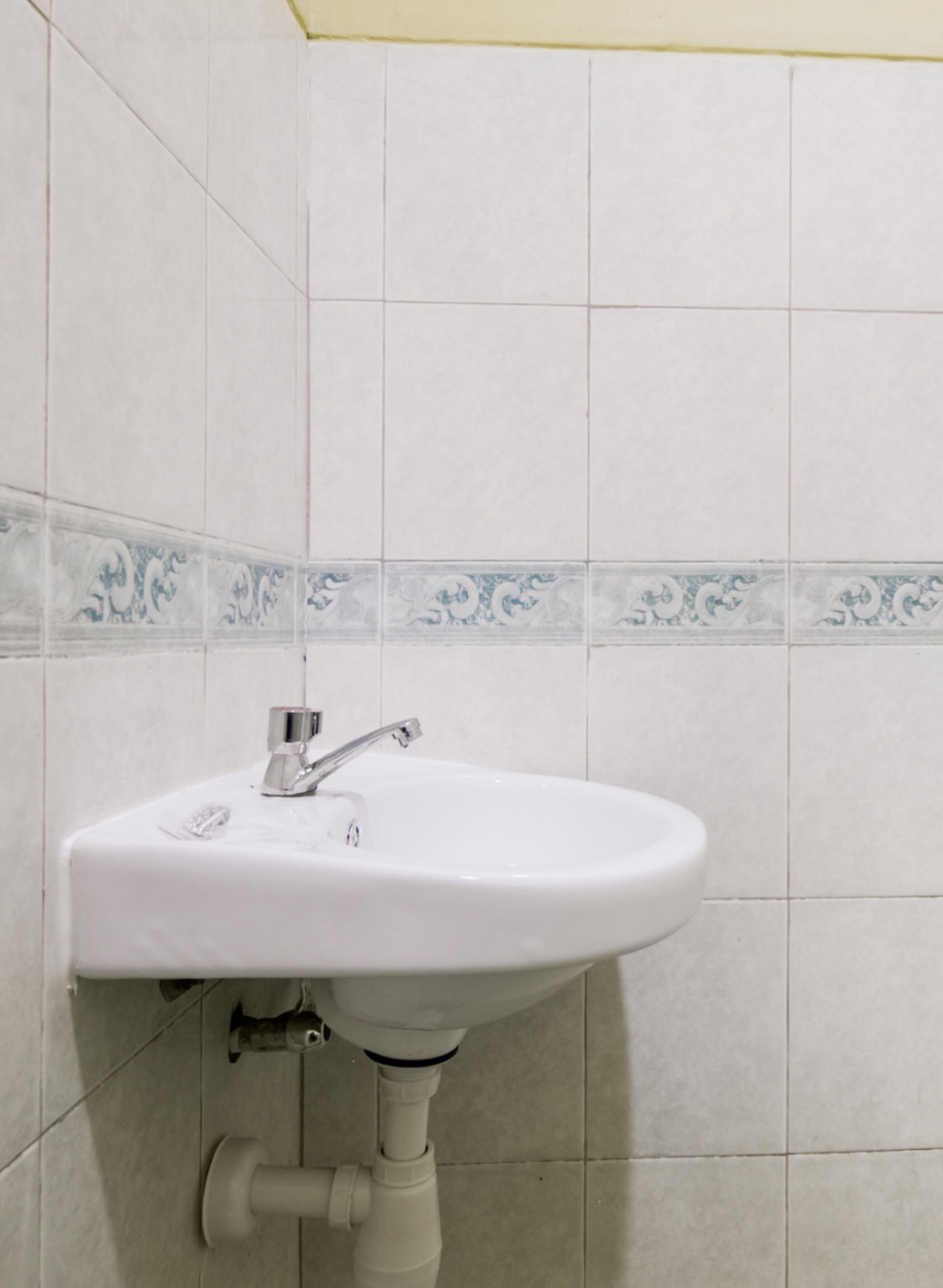 Un lavabo blanc pour salle de bain, doté d’un robinet chromé, fixé sur un mur carrelé orné d’une bordure décorative.
