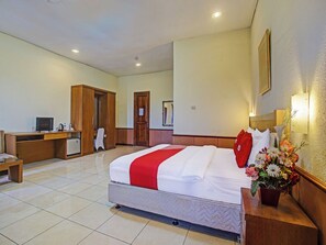 Une chambre d’hôtel équipée d’un lit, d’un bureau, d’une chaise, d’un petit réfrigérateur et d’un miroir au mur.