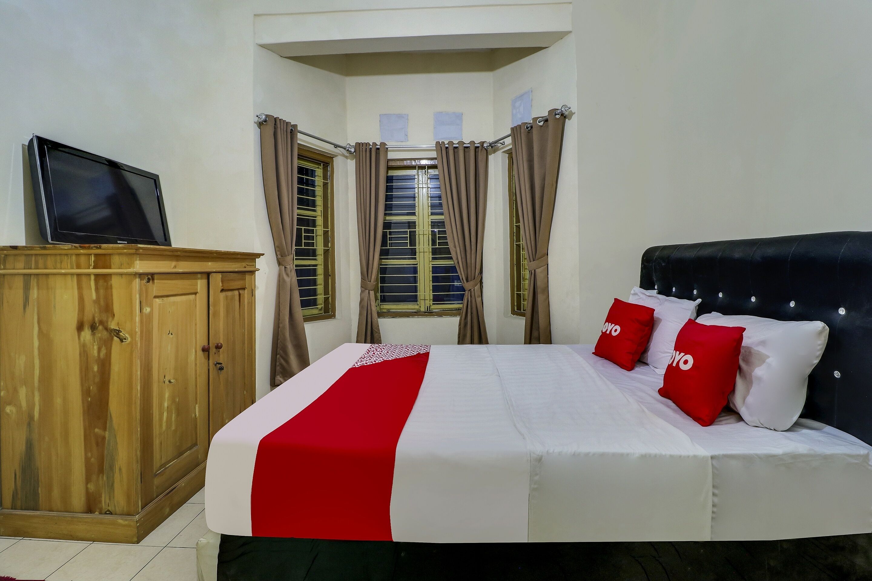 A neatly arranged bedroom with a bed, a wooden wardrobe, and a television on a stand.
