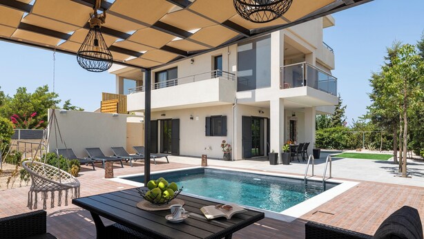 Een modern gebouw met twee verdiepingen, een zwembad, terras en een overdekte patio.
