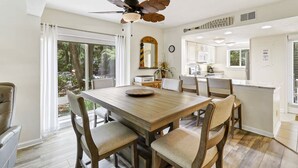 A dining area with a wooden table and chairs, a ceiling fan, and a view of the outdoors through large windows. - 302 Tanglewood Villa (Hilton Head Island)