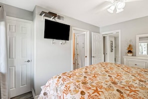 A bedroom with a bed, a television mounted on the wall, and a door leading to another room.
